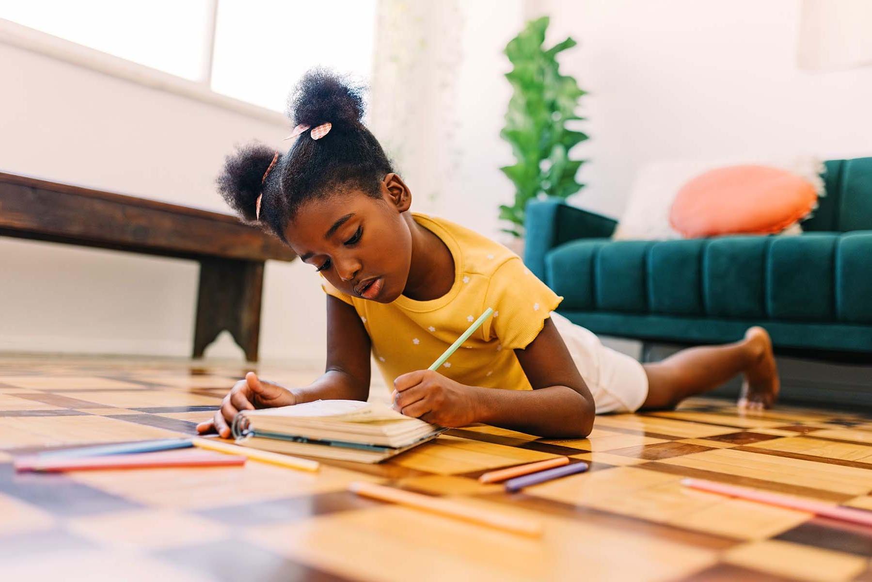 Child drawing on the floor with colored pencils.